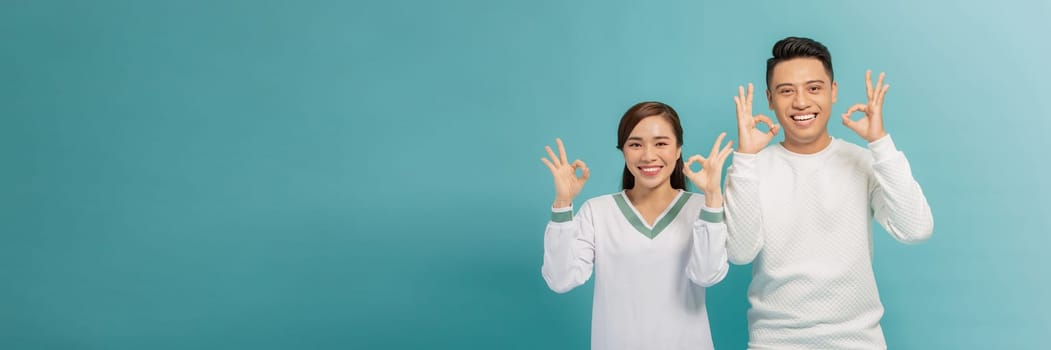 Young couple standing together smiling positive doing ok sign with hand and fingers
