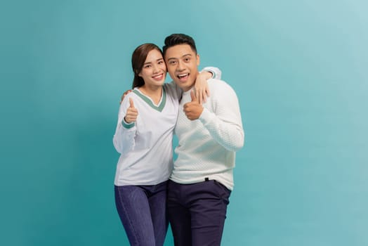 Pretty young couple standing isolated over blue background, showing thumbs up