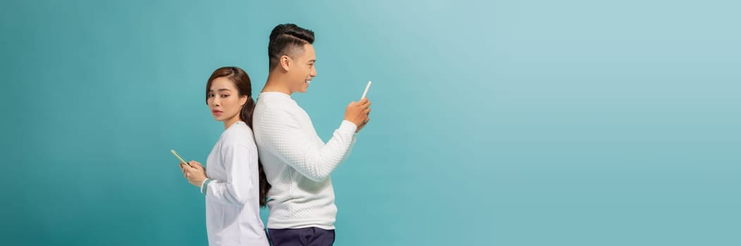 serious young couple standing back to back and text messaging over smart phones.