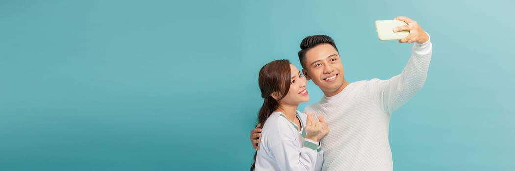 Happy young couple makes selfie, dressed in stylish clothes on light blue background