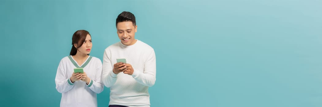 Asian young girl spying on her partner's mobile phone in blue background