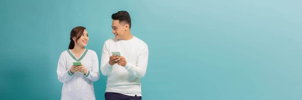 positive people man and woman smiling while gesturing at mobile phone isolated over light blue