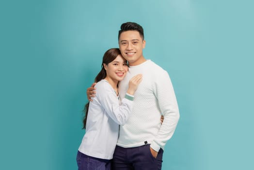 A happy young asian couple hugging while standing together and looking at camera