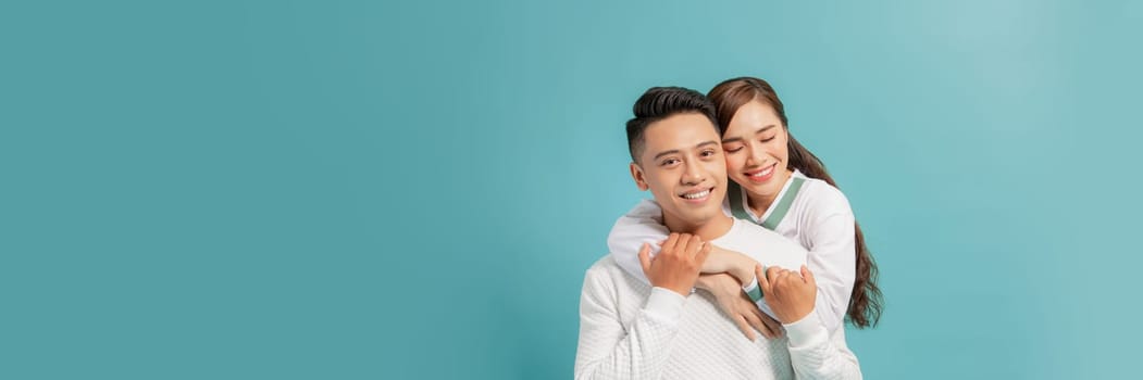 Attractive couple embracing and smiling on turquoise background