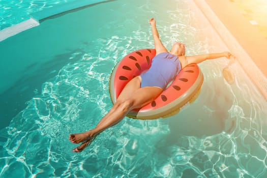 Happy woman in a swimsuit and sunglasses floating on an inflatable ring in the form of a watermelon, in the pool during summer holidays and vacations. Summer concept