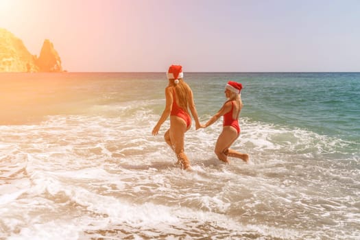 Women in Santa Claus hats run into the sea dressed in red swimsuits. Celebrating the New Year in a hot country.