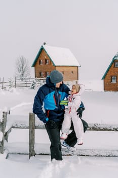 Smiling dad looking at little girl on his knees while sitting on a snowy fence. High quality photo