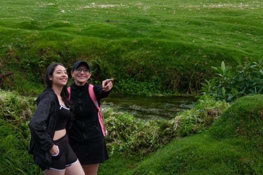 copyspace of mother pointing out a path to her daughter on a grassy green landscape next to a river. backpackers' day. High quality photo