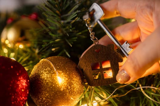 Gift key house with a keychain in hand backdrop of Christmas tree. Building, design, project, moving to new house, mortgage, rent and purchase real estate. A gift for New Year, Christmas
