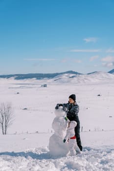 Mother and a little girl are making a snowman, standing in a snowy clearing. High quality photo