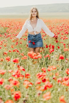 Happy woman in a poppy field in a white shirt and denim skirt with a wreath of poppies on her head posing and enjoying the poppy field