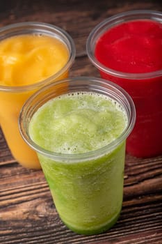 Three different fruit smoothies in plastic take away glasses on wooden background