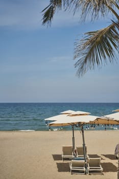 Straw sunshades and sunbeds on the empty pebble beach with sea in the background. Deserted beach with rattan sun loungers and umbrellas