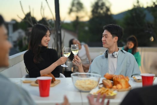Happy Asian male and female friends toasting champagne at a rooftop party