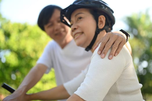 Loving senior couple having fun riding bicycle at in public park on a sunny day. Healthy lifestyle concept