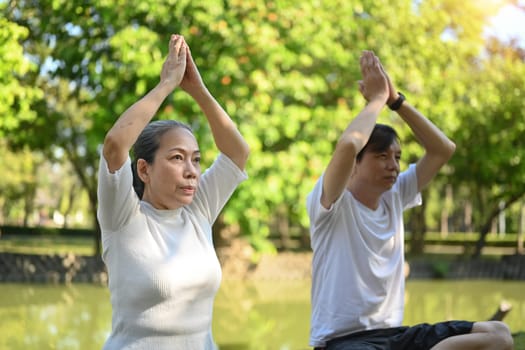 Older active couple doing breathing exercise in the summer park. Healthcare and meditation concept