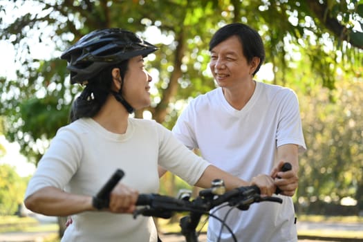 Cheerful middle aged couple riding bicycles in public park together. Healthy lifestyle concept