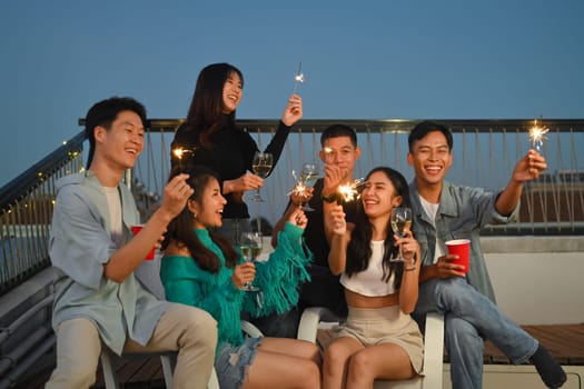 Group of young adult best friends having fun lighting sparklers during rooftop party