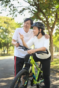 Happy Asian senior couple riding bicycles at summer park. Active retirement lifestyle concept