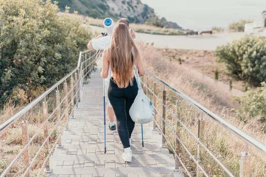 Happy Middle aged couple or friends practicing nordic walking in park near sea. Mature couple with trekking poles walking, practicing Nordic walking outdoors. Aging youthfully and sport concept.