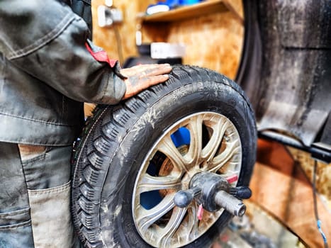 Ishim, Russia - November 27, 2023: Mechanic repairs a car wheel and makes a tire in a dirty garage. Replacement of summer wheels, tires for winter indoors