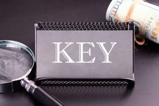 KEY text on the business card next to the money, a magnifying glass on a black background