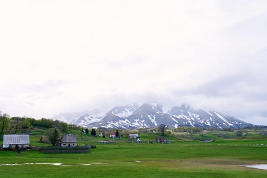 Village in a green valley at the foot of foggy snowy mountains. High quality photo