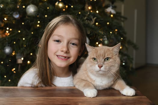 A girl near a ginger cat near the christmas tree