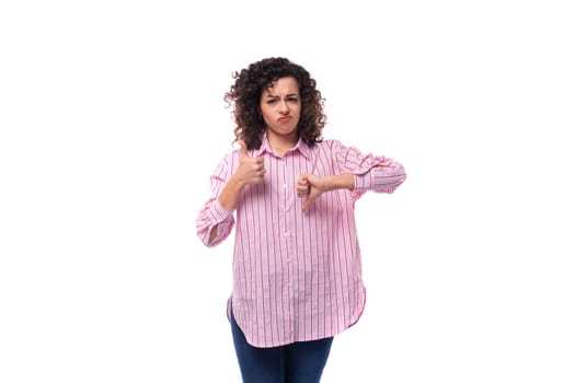 young curly brunette model woman dressed in a pink striped shirt shows like and dislike.