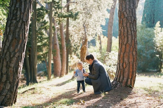 Mom squatted down in front of a little girl on a path in the forest. High quality photo