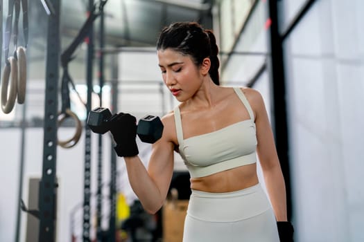 Pretty Asian sport woman hold and lift dumbbell up with one hand and look to equipment in fitness gym and look concentrate to training.