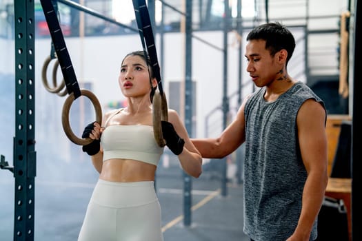 Asian coach or trainer man help and support sport woman to exercise with loop in fitness gym and also show example of good position of training.