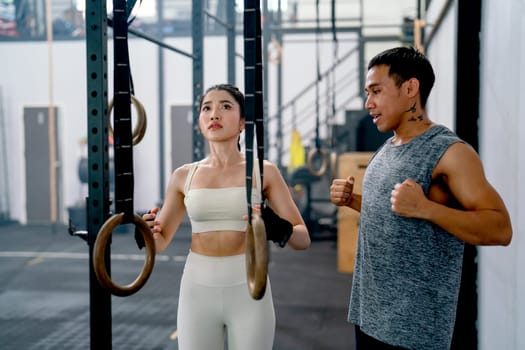 Asian coach or trainer man help and support sport woman to exercise with loop in fitness gym and also show example of good position of training.