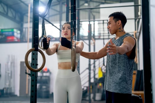 Asian coach or trainer man help and support sport woman to exercise with loop in fitness gym and also show example of good position of training.