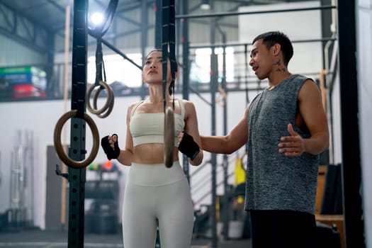 Asian coach or trainer man help and support sport woman to exercise with loop in fitness gym and also show example of good position of training.