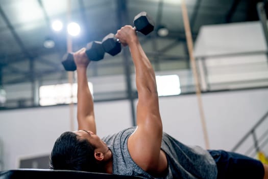 Close up sport man lift dumbells up to over head during lie on long chair in fitness gym.
