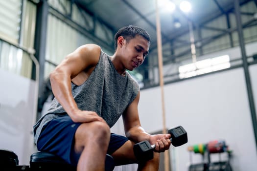 Asian sport man sit and hold dumbbell on chair in fitness gym and look relax after train the body for healthy lifestyle.