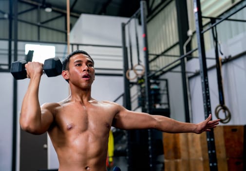 Asian sport man hold dumbbell with one hand and stay on position of exercise or training in fitness gym.