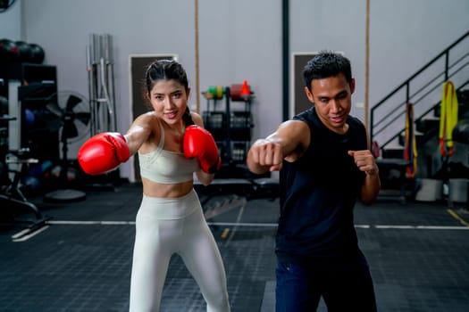 Wide shot of Asian sport trainer man help woman to practice with boxing to punch and hit for good action and movement in fitness gym.