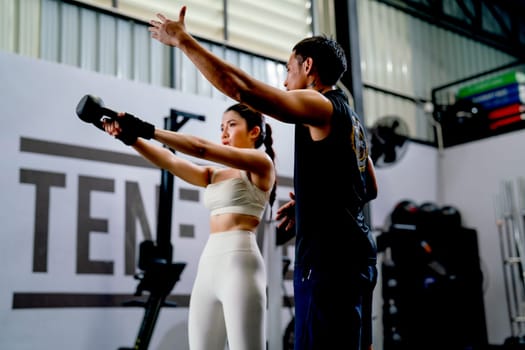 Asian sport woman hold weight to exercise with support by the trainer in fitness gym.