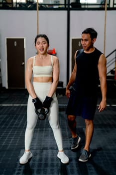 Asian sport woman hold weight to exercise with support by the trainer in fitness gym.