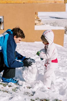 Little girl and her dad are making a snowman in the yard of a wooden house. High quality photo