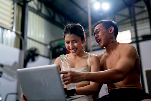 Asian sport man and woman look fun during enjoy with laptop in fitness gym.