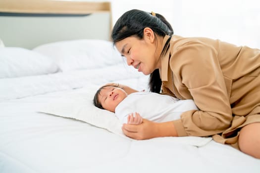 Asian mother lie beside of newborn baby sleep on bed in bedroom with day light and they look relax and happiness.