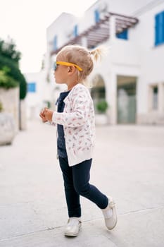 Little girl in sunglasses stands half-turned in the courtyard of the house. High quality photo