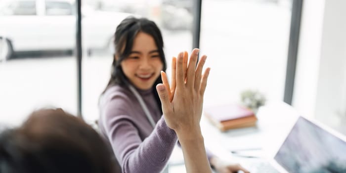 Successful business people giving each other a high five in a meeting. Two young business celebrating teamwork in an office.