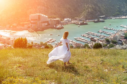 Happy woman in a white dress and hat stands on a rocky cliff above the sea, with the beautiful silhouette of hills in thick fog in the background