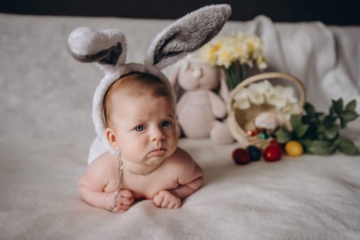 Cute little baby wearing bunny ears for Easter. Near Easter eggs. looks into the camera and gets angry. High quality photo