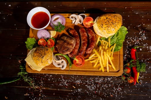 fast food burger potatoes fries sausages cutlets ketchup tomatoes onions peppers mushrooms on a wooden board on the table top view barbecue mix