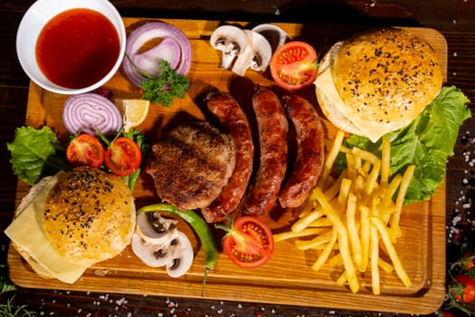 fast food burger potatoes fries sausages cutlets ketchup tomatoes onions peppers mushrooms on a wooden board on the table top view barbecue mix